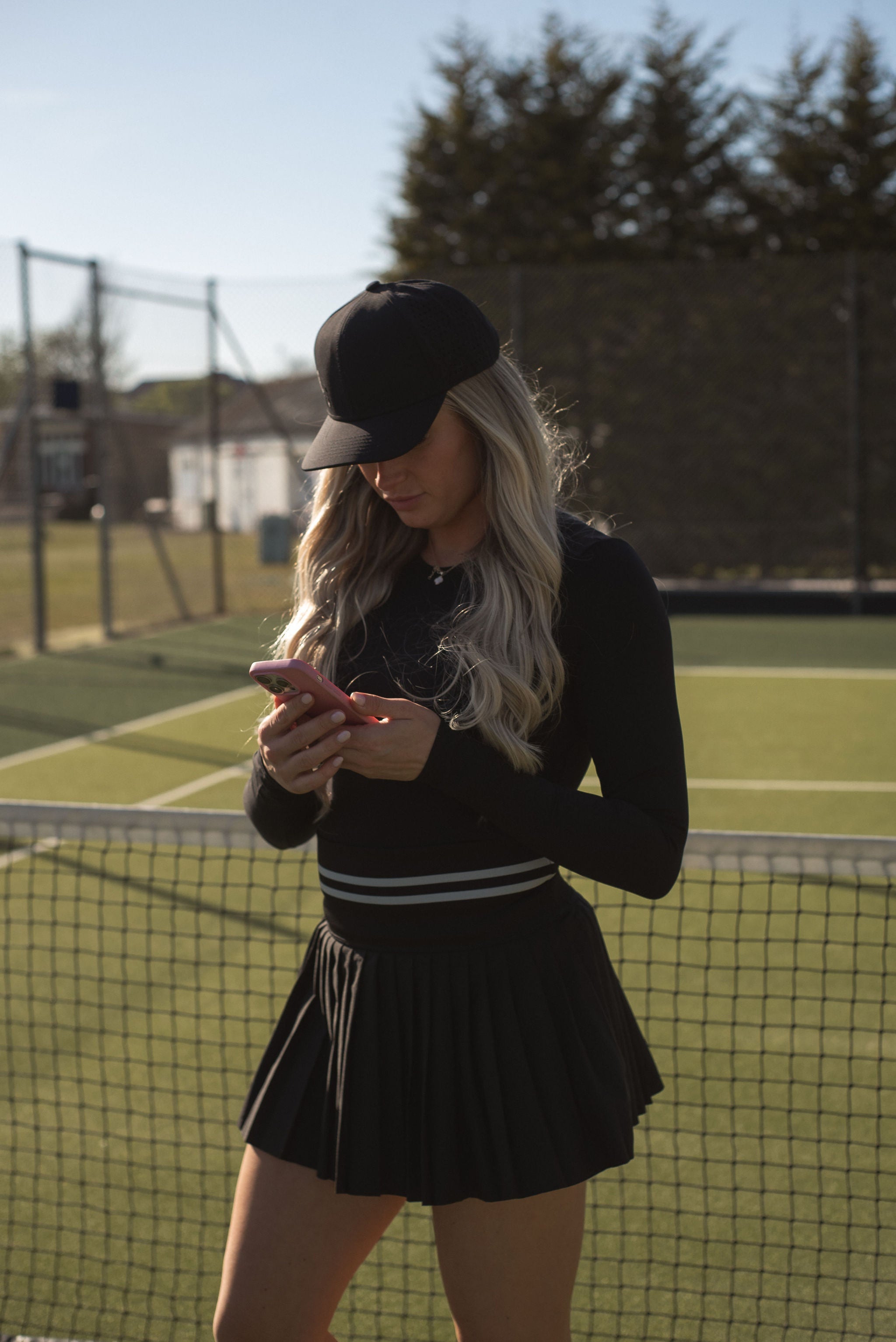 women on tennis court using her phone wearing LOST tennis or padel skort