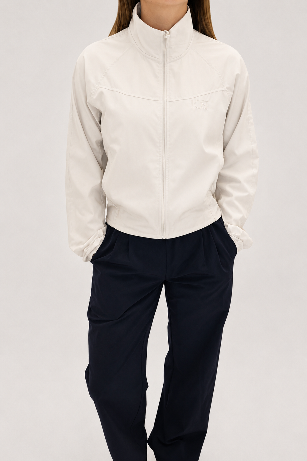 Person wearing a white jacket and dark pants on a light gray background