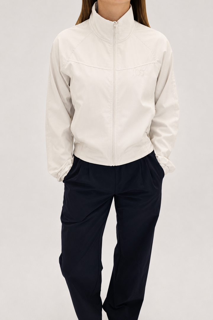 Person wearing a white jacket and dark pants on a light gray background